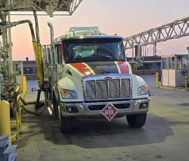 OilWorks flatbed fuel delivery truck parked inside a construction site with lights on and water reflections on the concrete floor.