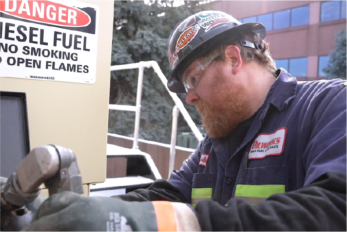 Fuel technician servicing commercial fueling equipment while wearing proper safety gear.
