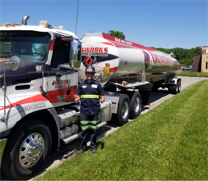 Fuel delivery driver standing beside a bulk fuel tanker truck during a commercial delivery.